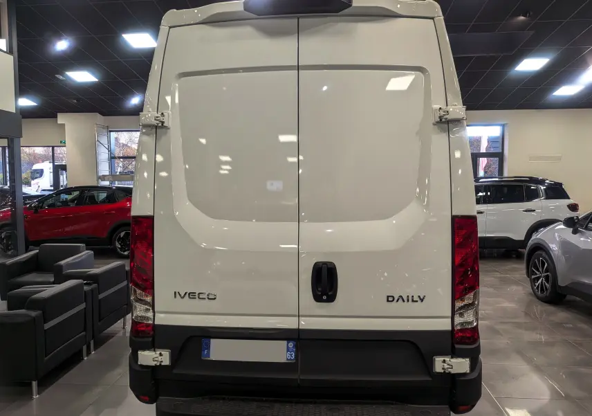 Vue arrière d'un fourgon blanc Iveco Daily 2025 dans un showroom, avec portes battantes fermées et feux rouges visibles.