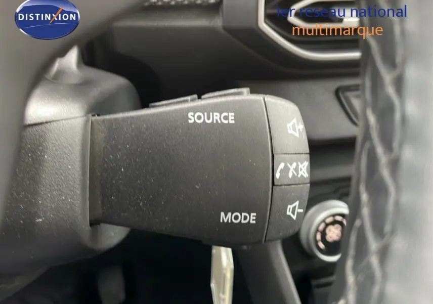 Gros plan sur la commande audio au volant d’un Dacia Jogger kaki lichen, intérieur noir visible en arrière-plan.