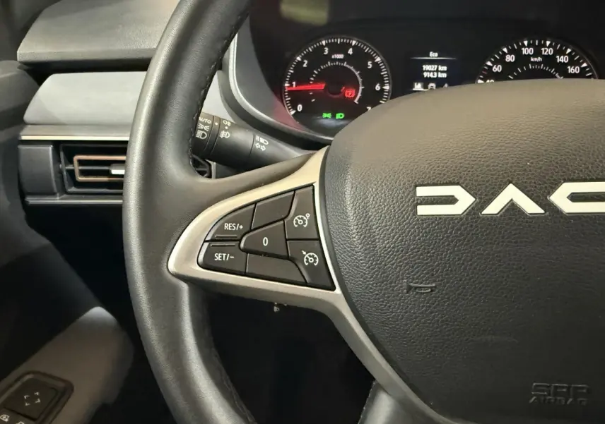 Gros plan sur le volant cuir synthétique de la Dacia Sandero 2024 avec commandes régulateur et tableau de bord éclairé.