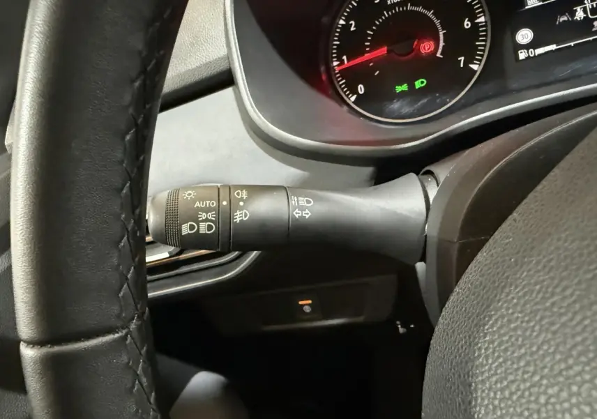 Gros plan sur la manette de phares à gauche du volant noir du tableau de bord du Dacia Sandero 2024.
