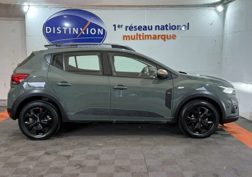 Vue de profil côté gauche d'une Dacia Sandero Extreme+ TCe 110 2024 en vert avec jantes noires et barres de toit assorties.