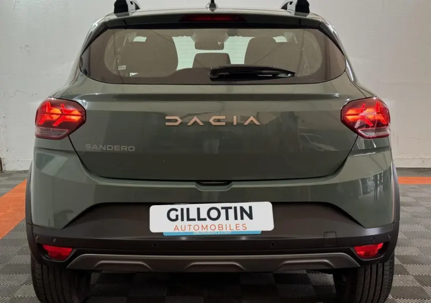 Vue arrière d'une Dacia Sandero Extreme+ TCe 110 2024 en vert avec feux LED allumés et barres de toit grises.