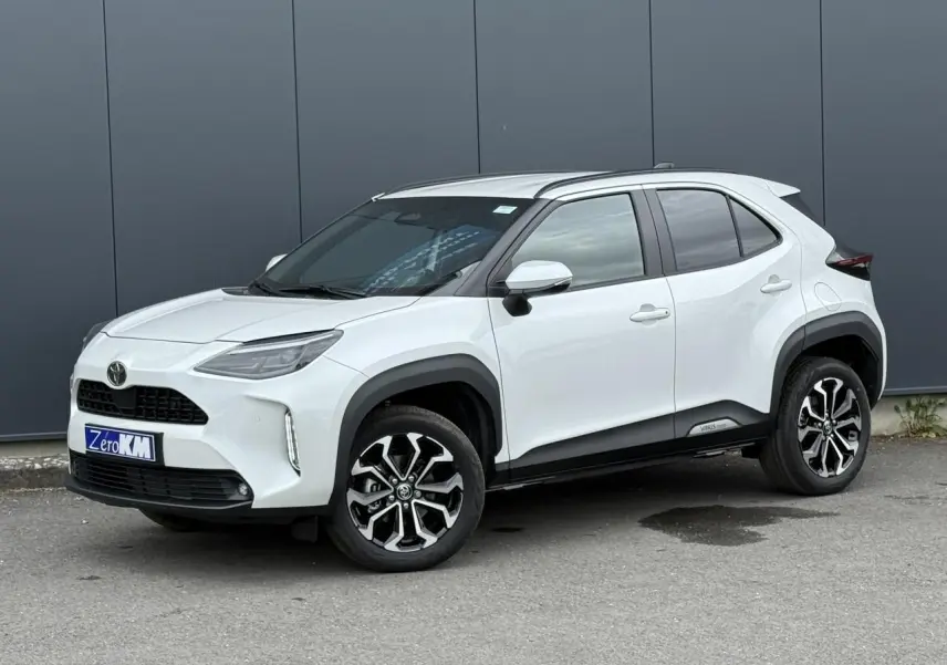 Toyota Yaris Cross blanc lunaire vue 3/4 avant droit, avec jantes alliage et protections noires contrastées.