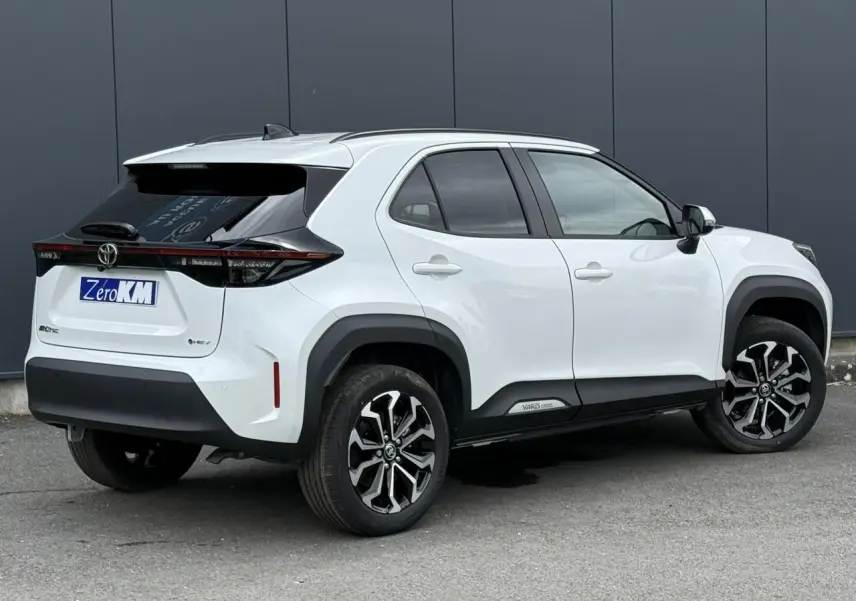 Vue 3/4 arrière droite de la Toyota Yaris Cross 1.5 Hybrid blanche avec toit noir et jantes alliage bicolores.