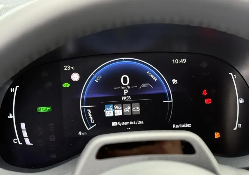 Vue rapprochée du tableau de bord numérique de la Toyota Yaris Cross blanc lunaire, affichant 0 km/h et indicateurs hybrides actifs.