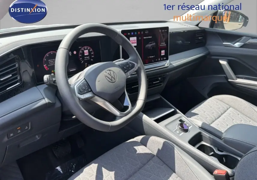 Vue intérieure du Volkswagen Tiguan 2026 montrant le tableau de bord et le volant avec écran tactile et sellerie grise.