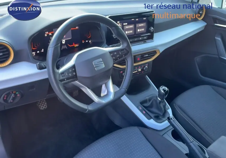 Vue intérieure côté conducteur du tableau de bord et volant du SEAT Arona blanc, avec sellerie tissu noire et console centrale.