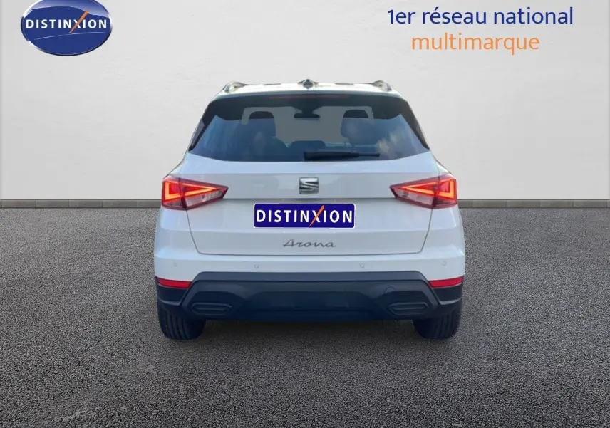 Vue arrière d'un SEAT Arona blanc avec toit gris, feux arrière allumés et double sortie d'échappement intégrée.