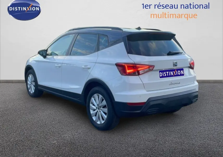 Vue 3/4 arrière droite d’un SEAT Arona blanc avec toit gris, feux arrière allumés et jantes argentées.