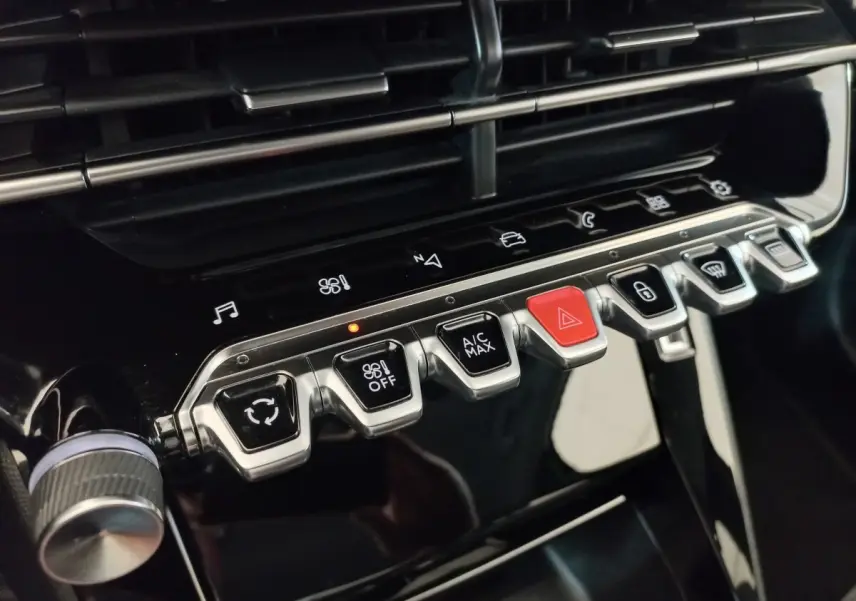 Gros plan sur les commandes centrales noires et chromées du tableau de bord de la Peugeot 208 PureTech 100 noir, avec bouton rouge d’alerte.