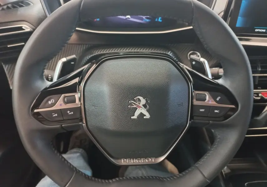 Vue rapprochée du volant cuir noir de la Peugeot 208 2022 avec commandes multifonctions et logo central.