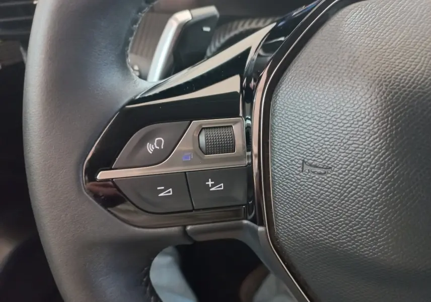 Gros plan sur les commandes gauche du volant cuir noir de la Peugeot 208 PureTech 100 Allure Pack 2022.