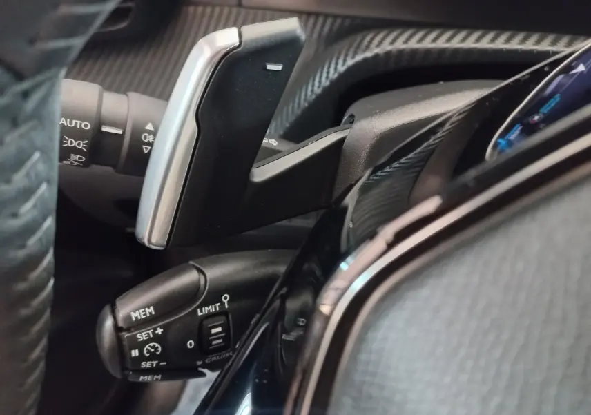Gros plan sur la commande de régulateur de vitesse et palettes au volant du tableau de bord noir d’une Peugeot 208 2022.