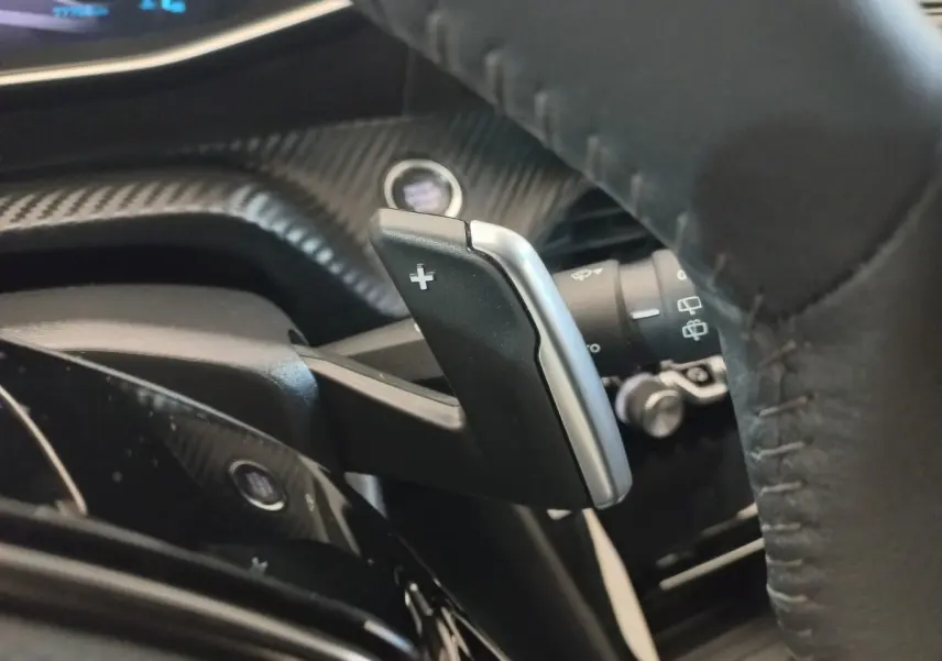 Gros plan sur la palette de changement de vitesse droite en plastique noir et argent, volant cuir noir de la Peugeot 208 2022.