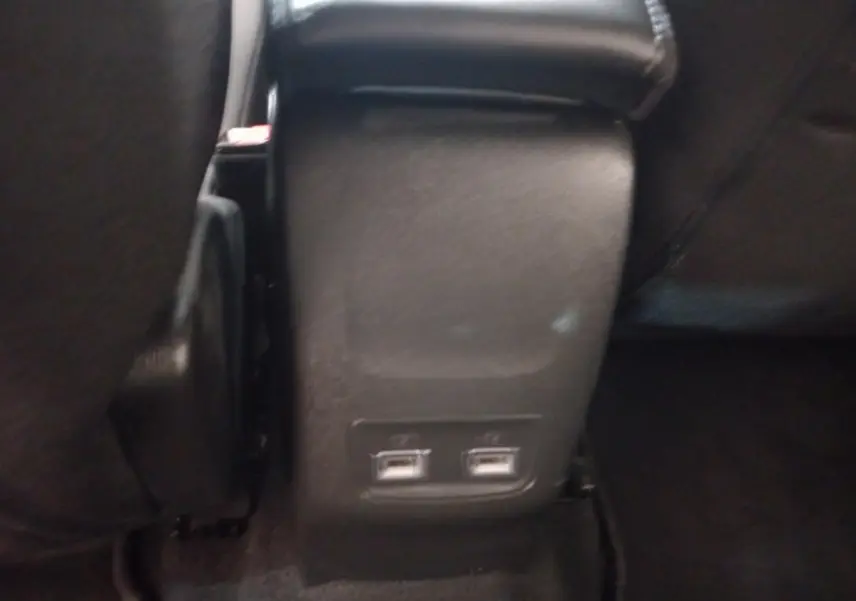 Gros plan sur la console arrière noire de la Peugeot 208 avec deux ports USB visibles au bas des sièges avant.