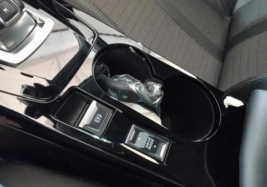 Gros plan sur la console centrale noire brillante de la Peugeot 208 PureTech 100, avec boutons frein à main et mode de conduite.