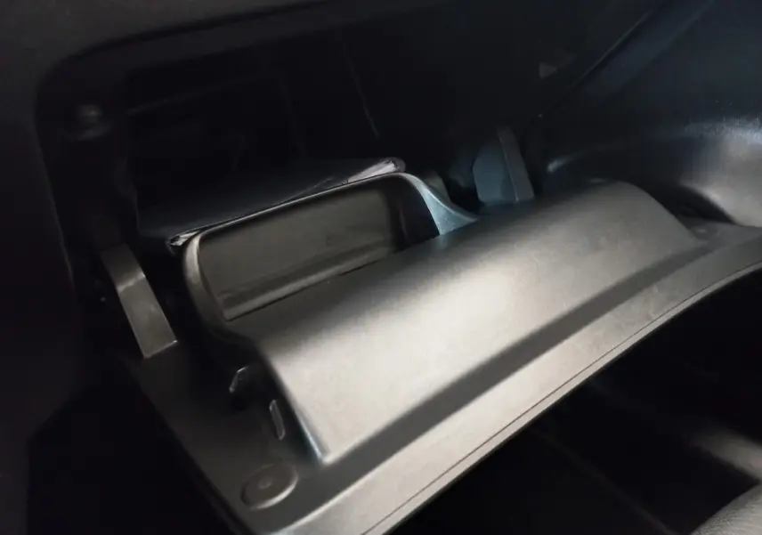Gros plan sur la boîte à gants ouverte de la Peugeot 208 noire, intérieur sombre avec documents visibles.