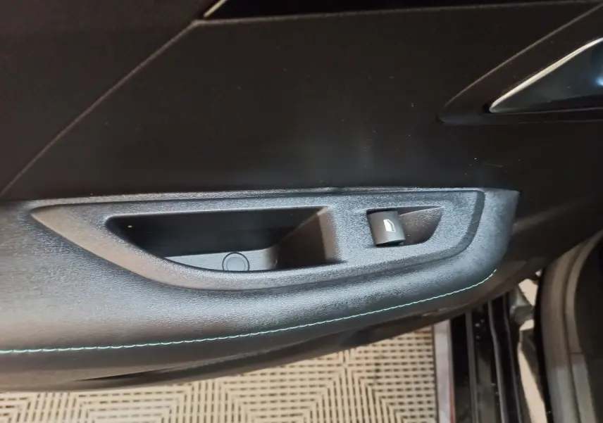 Détail de la poignée intérieure de porte côté gauche d’une Peugeot 208 noire, avec bouton de verrouillage.
