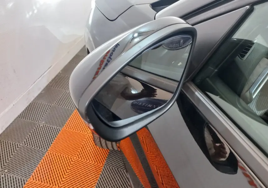 Rétroviseur côté gauche d’une Peugeot 208 noire, vue rapprochée avec reflet du sol orange et gris.