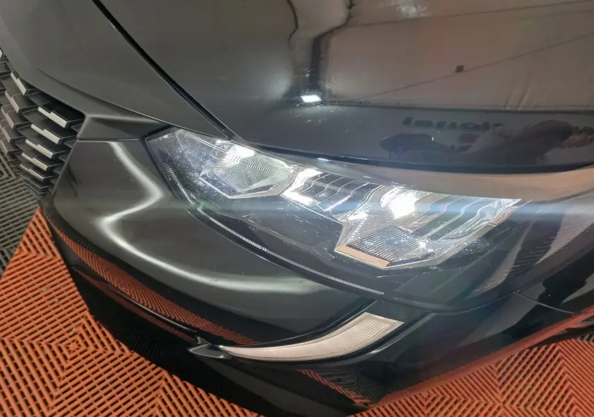 Gros plan sur le phare avant gauche noir brillant de la Peugeot 208 PureTech 100 S&S EAT8 Allure Pack 2022.