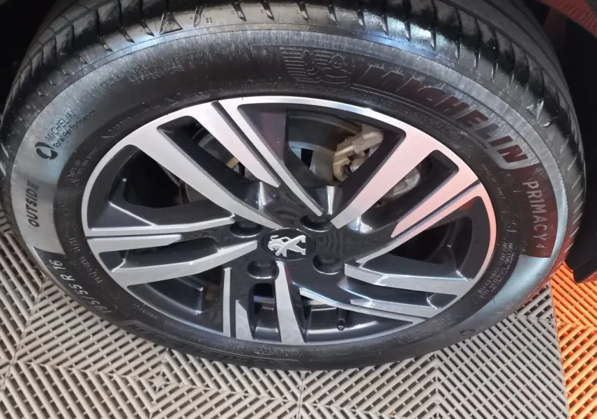 Gros plan sur la jante alliage noire et argentée d'une Peugeot 208 noire, avec pneu Michelin visible.