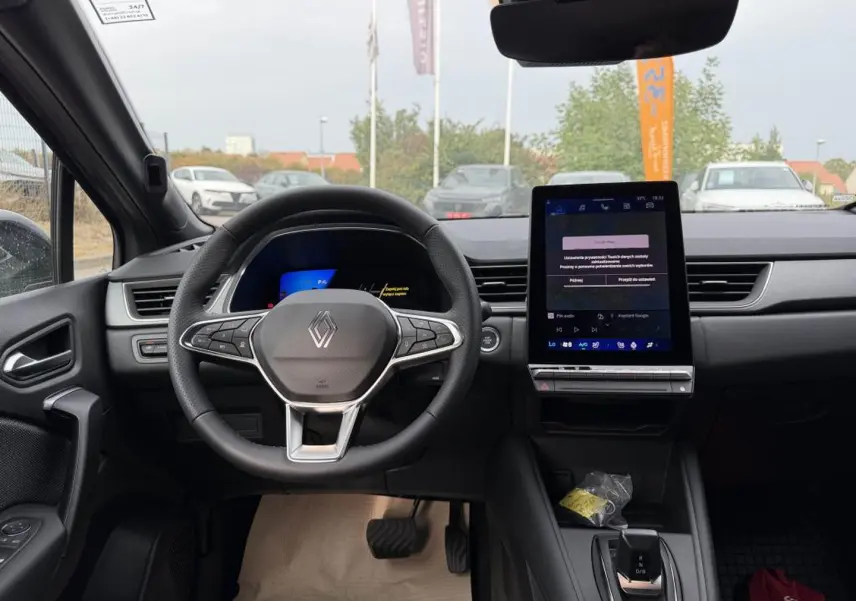 Vue intérieure avant du tableau de bord gris cassiopé du Renault Symbioz 1.8 e-tech avec écran tactile vertical et volant multifonction.