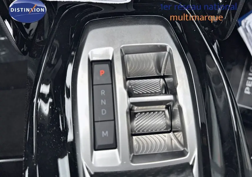Gros plan sur la console centrale noire métallisée du Peugeot 2008 Hybrid 136ch avec sélecteur de boîte automatique et boutons de vitesse.