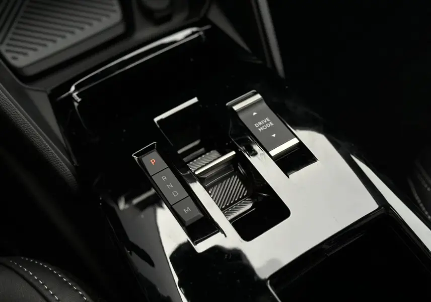 Gros plan sur la console centrale noire brillante de la Citroën C4 NV Hybrid 2025 avec sélecteur de boîte auto et bouton Drive Mode.