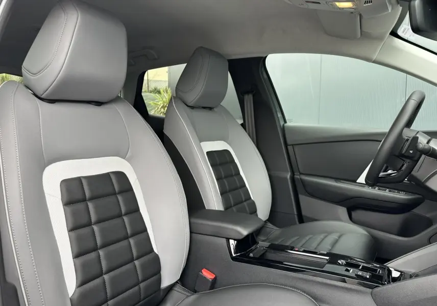 Vue intérieure côté droit des sièges avant gris clair et noir de la Citroën C4 NV Hybrid 2025 avec accoudoir central et volant noir.