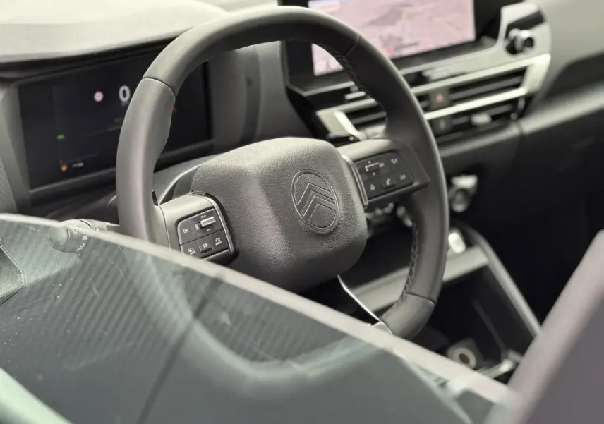 Vue rapprochée du volant cuir noir de la Citroën C4 NV Hybrid 2025 avec tableau de bord numérique et écran tactile central.