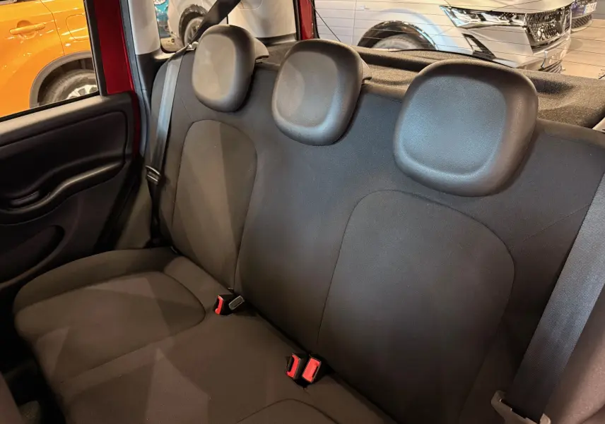 Vue intérieure sur la banquette arrière noire en tissu de la Fiat Panda 1.0 Hybrid Rouge Amore, avec appuie-têtes et ceintures visibles.