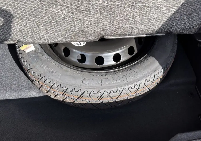 Gros plan sur la roue de secours noire dans le coffre du Renault Symbioz gris clair, visible sous la banquette arrière.