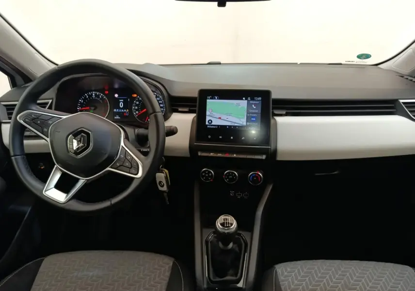 Vue intérieure avant de la Renault Clio blanche 2023, tableau de bord avec écran tactile et volant multifonctions en cuir synthétique.