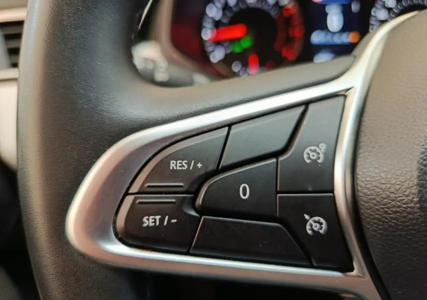 Gros plan sur les commandes du régulateur de vitesse au volant cuir synthétique de la Renault Clio blanche 2023.