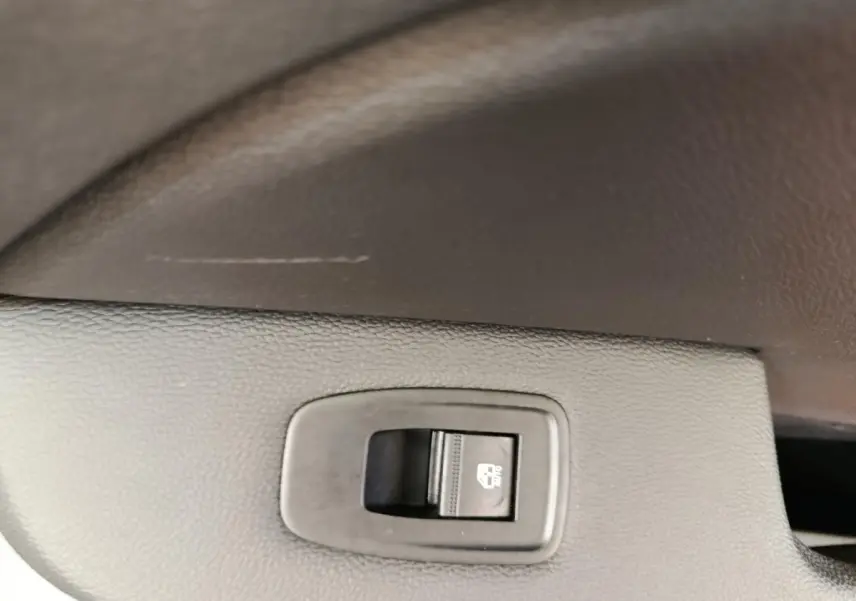 Gros plan sur le bouton de verrouillage des vitres arrière dans l’habitacle noir de la Renault Clio blanche.