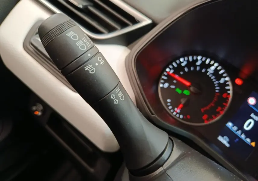 Gros plan sur la manette de commandes des phares et clignotants dans l'habitacle d'une Renault Clio blanche 2023.