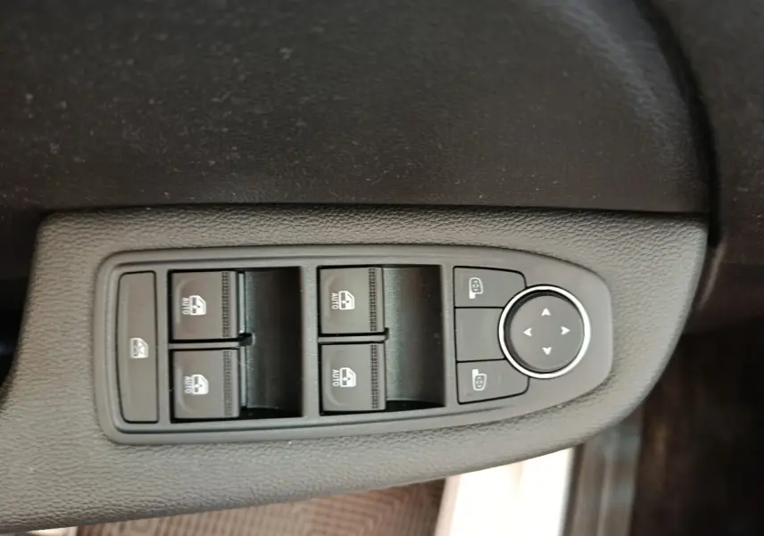 Gros plan sur les commandes de lève-vitres et rétroviseurs côté conducteur d’une Renault Clio blanche 2023.