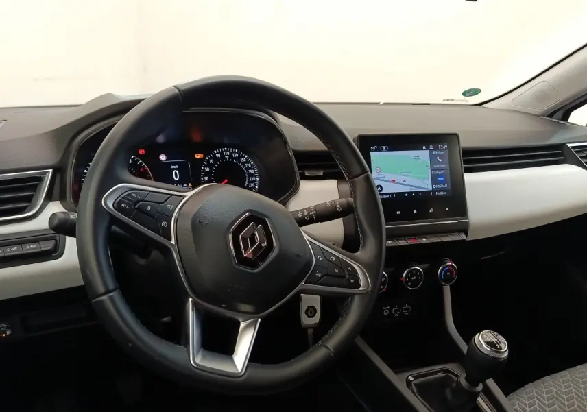 Vue intérieure de face du tableau de bord de la Renault Clio blanche, avec volant cuir, écran tactile et levier de vitesses manuel.