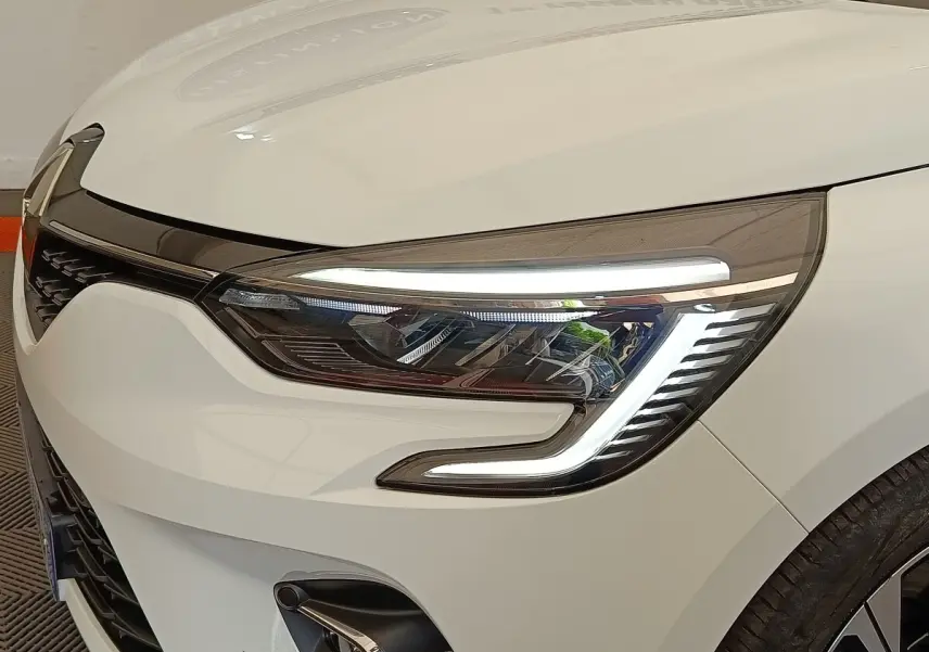 Gros plan sur le phare avant droit allumé d'une Renault Clio blanche Evolution TCe 100 GPL de 2023.