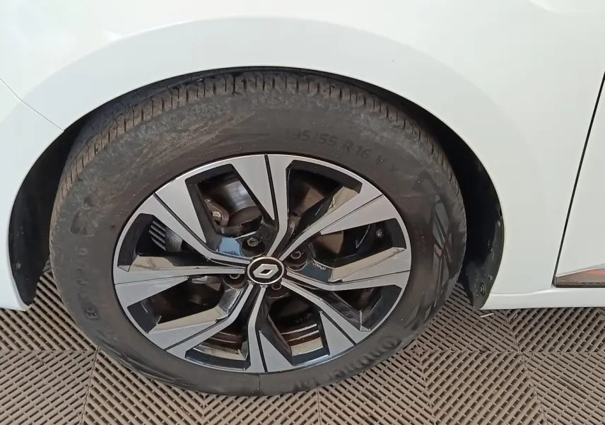 Gros plan sur la roue avant droite d’une Renault Clio blanche, avec jante alliage bicolore au design moderne.