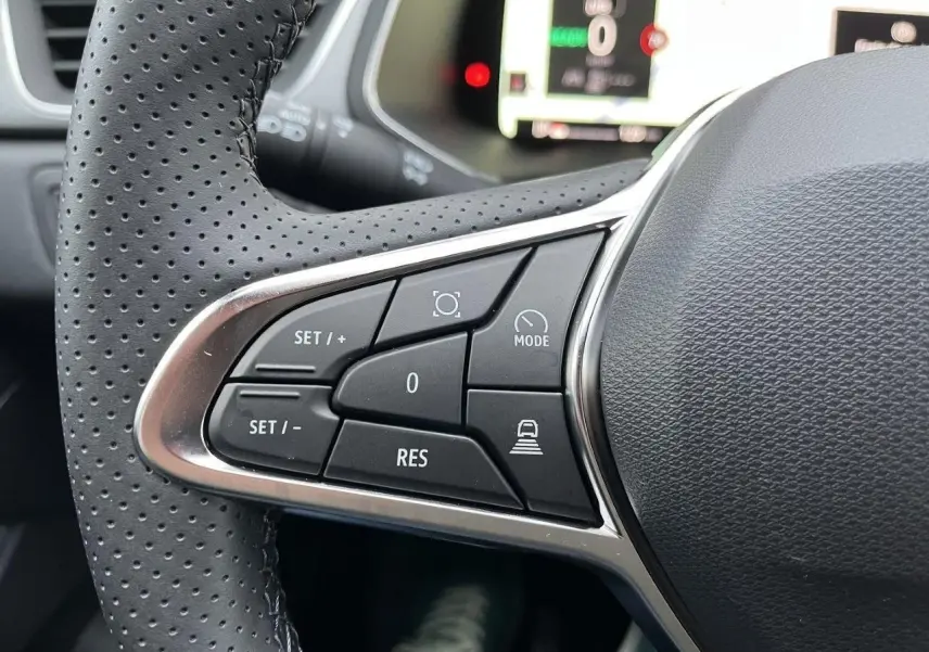 Gros plan sur les commandes au volant gauche du Renault Captur gris Cassiopée, version hybride 2025, avec boutons multifonctions.