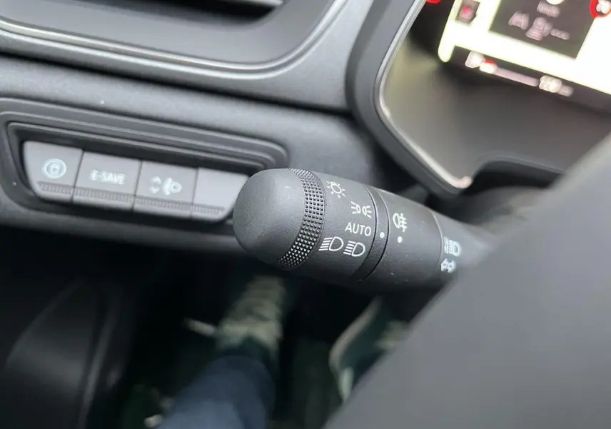 Gros plan sur la manette des feux du tableau de bord d’un Renault Captur gris Cassiopée, intérieur moderne et écran digital partiel visible.