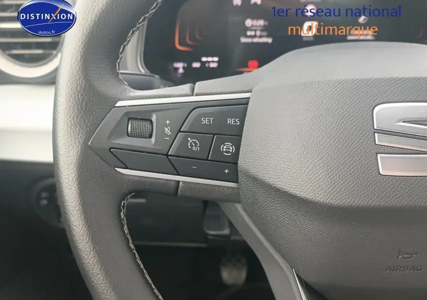 Gros plan sur le volant cuir noir multifonction avec logo SEAT et commandes de régulateur de vitesse.