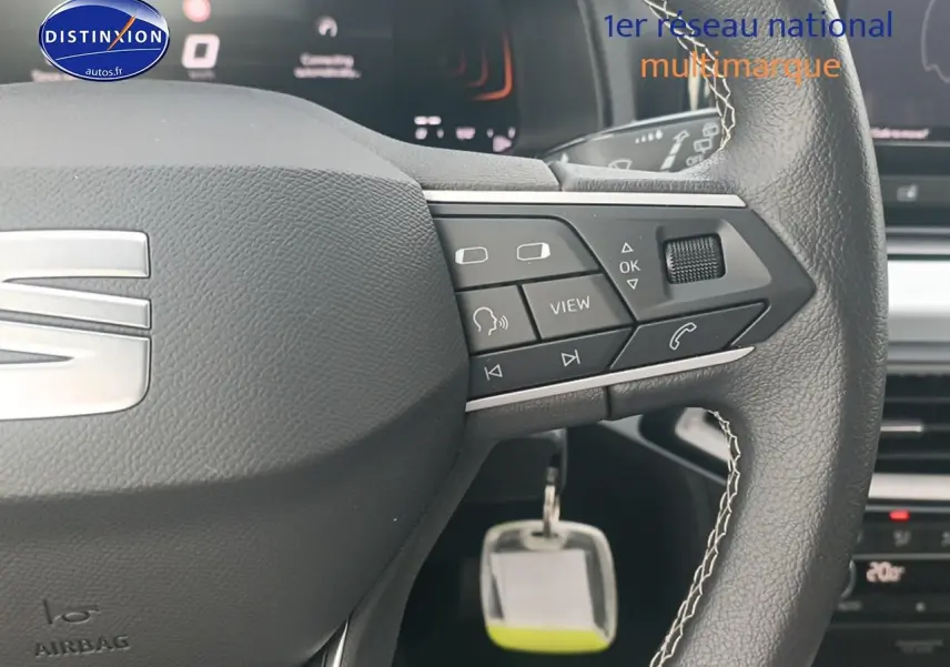 Gros plan sur le volant cuir noir de la SEAT Ibiza blanc Nevada, avec commandes multifonctions et logo satiné visible.