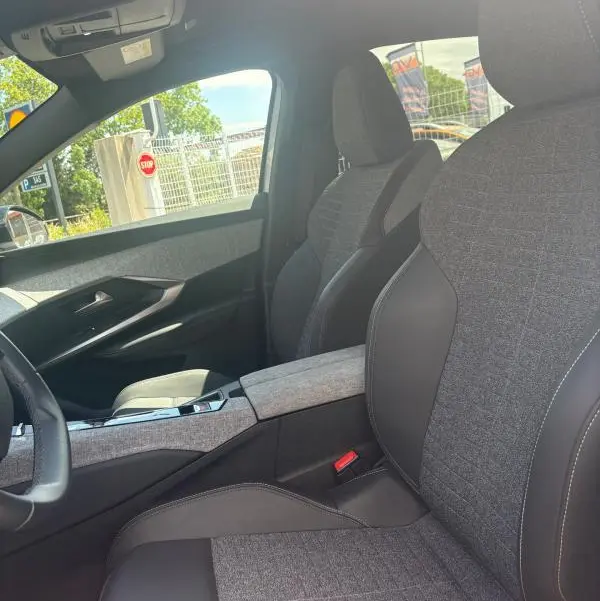 Intérieur du Peugeot 3008 Hybrid 136 e-DCS6 Allure 2025, vue côté conducteur sur sièges tissu gris clair et cuir noir.