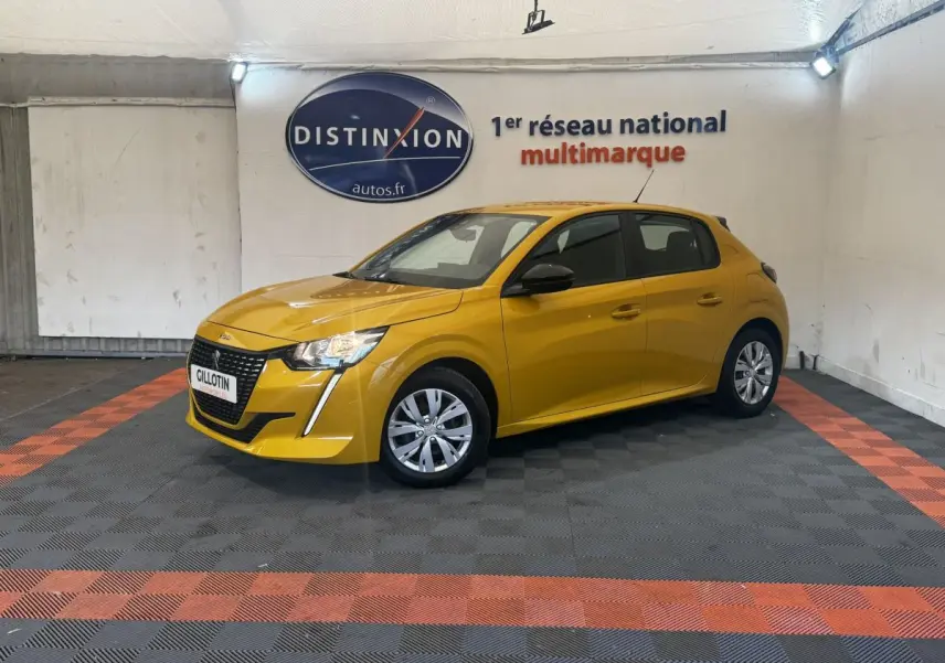 Peugeot 208 jaune vue 3/4 avant droit, avec calandre noire et feux LED, stationnée en intérieur sur sol damier noir et orange.