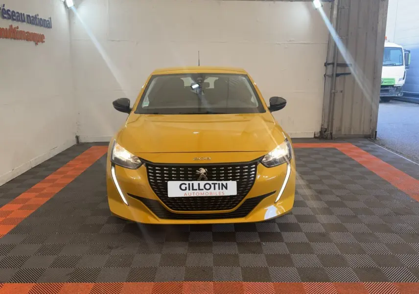 Vue frontale d'une Peugeot 208 jaune vif avec feux LED allumés, dans un espace intérieur de présentation.