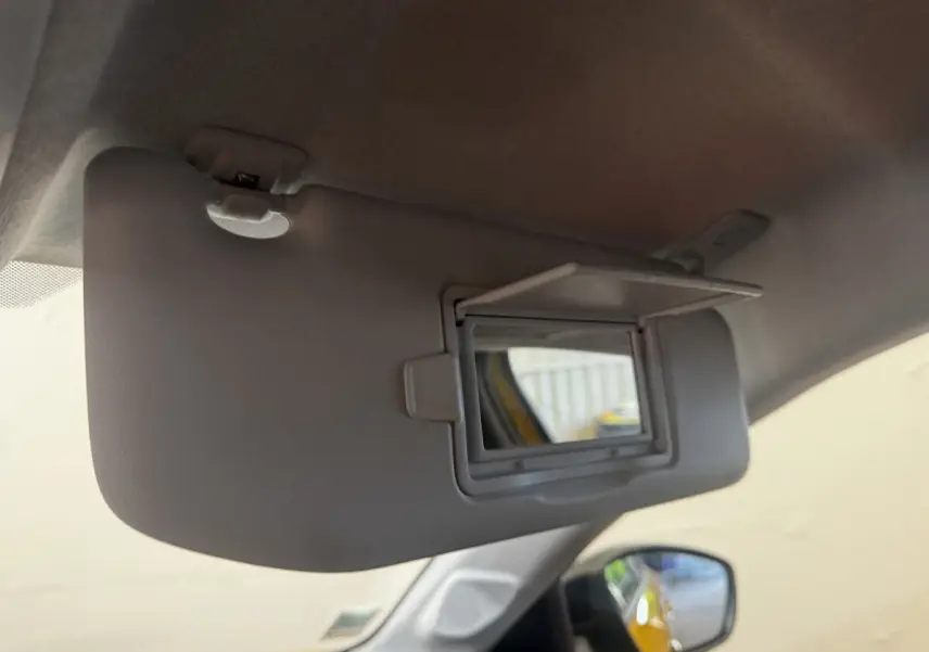 Détail du pare-soleil côté conducteur avec miroir de courtoisie ouvert dans une Peugeot 208 jaune visible en reflet.