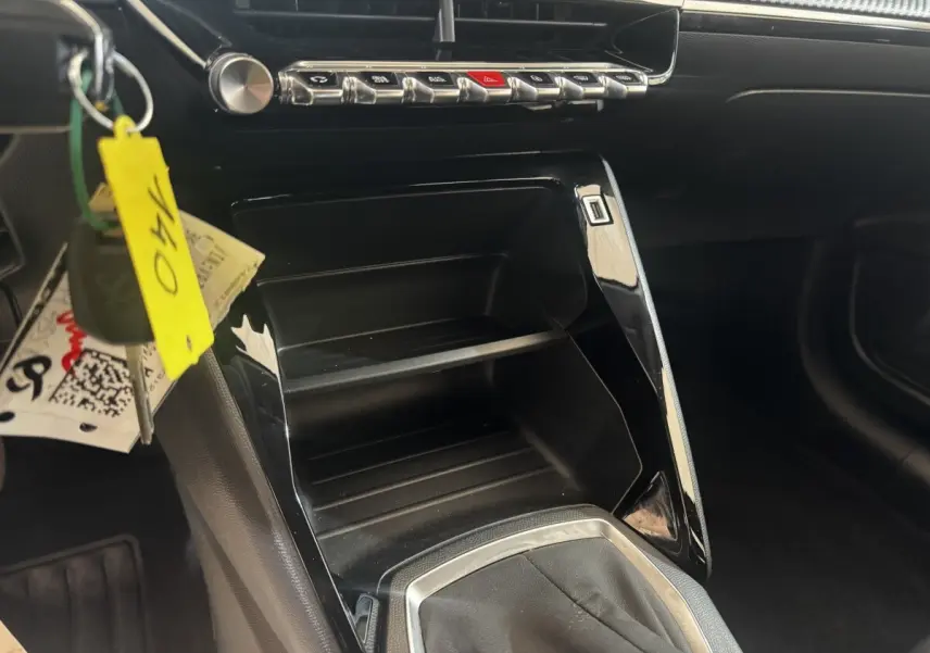 Vue intérieure centrée sur la console centrale noire brillante de la Peugeot 208 jaune, avec clés suspendues visibles.