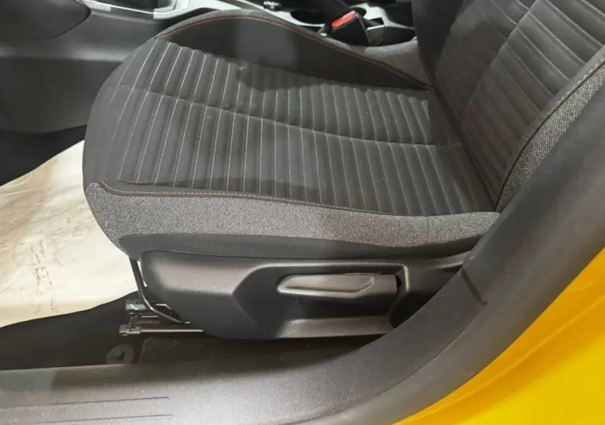 Gros plan sur le siège avant gauche noir avec surpiqûres rouges, porte ouverte d'une Peugeot 208 jaune.